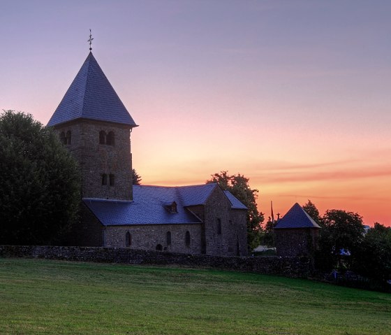 Eine Kirche mit Turm vor einem farbenfrohen Sonnenuntergang, umgeben von Bäumen und einer Wiese., © Naturpark Südeifel, C. Schleder Eine Kirche mit Turm vor einem farbenfrohen Sonnenuntergang, umgeben von Bäumen und einer Wiese., © Naturpark Südeifel, C. Schleder