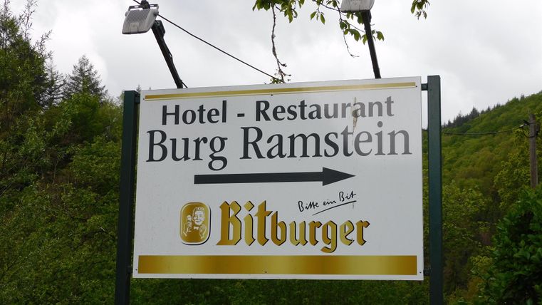 Ein Schild für das Hotel-Restaurant Burg Ramstein. Es zeigt einen Pfeil nach links und wirbt für Bitburger Bier.