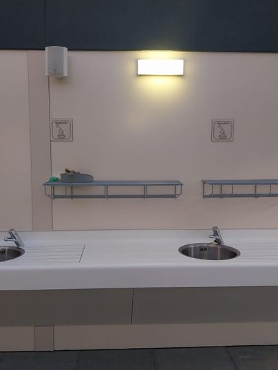 Ein modernes Waschbecken mit zwei Spülbecken an einer weißen Wand. Oben sind zwei Regale zur Ablage vorhanden.