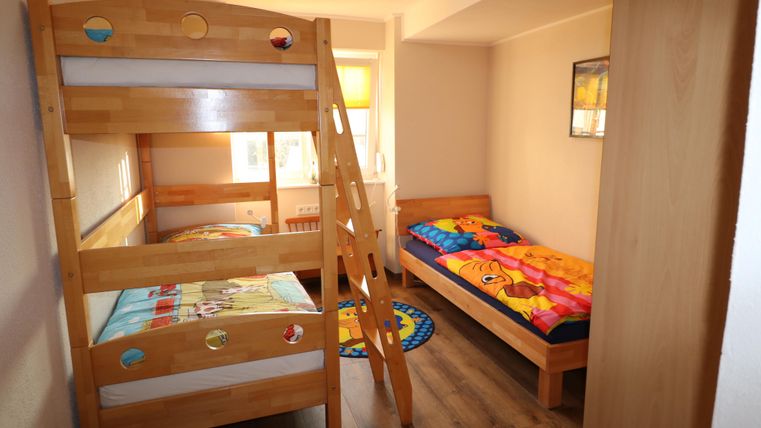 Ein Kinderzimmer mit einem Etagenbett aus Holz und einem Einzelbett. Bunte Bettwäsche und ein runder Teppich sorgen für eine freundliche Atmosphäre.