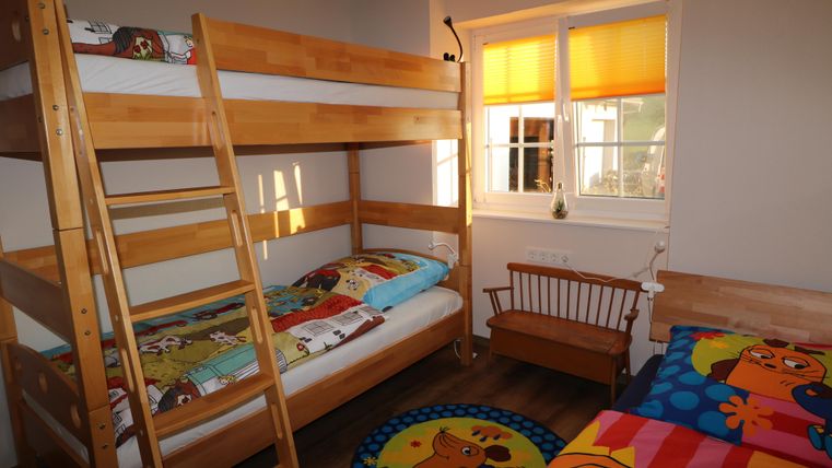 Ein farbenfrohes Kinderzimmer mit einem Etagenbett und zwei Einzelbetten. Die Wände sind hell, und das Fenster lässt viel Tageslicht herein.