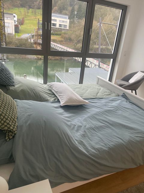 Ein modernes Schlafzimmer mit einem großen Fenster und mit einem wunderschönen Blick in die Natur. Bettwäsche ist vorhanden.