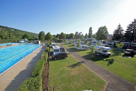 Ein Campingplatz mit Wohnmobilen neben einem Schwimmbad. Die Umgebung ist grün und einladend, ideal für Familienausflüge.