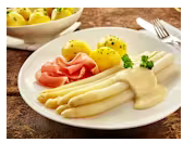 Ein Teller mit weißem Spargel, serviert mit gekochten Kartoffeln und Schinken. Dazu gibt es eine cremige Sauce.