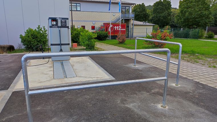 Eine moderne Tankstelle mit einem Pumpstand und einem abgesperrten Bereich. Im Hintergrund sind Gebäude und Bäume zu sehen.