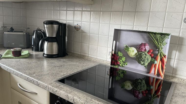 Eine moderne Küche mit einem Kochfeld und einem schönen Bild von frischen Gemüse. Im Hintergrund sind Küchengeräte und eine saubere Arbeitsfläche sichtbar.