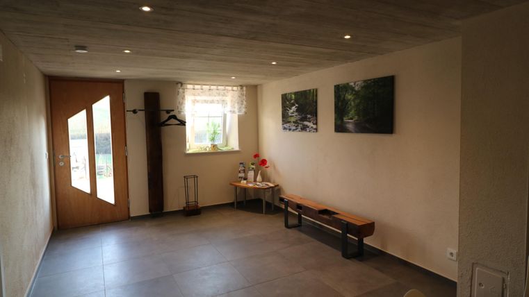 Ein gemütlicher Eingangsbereich mit einem Holzfußboden und einer großen Fensterfront. An der Wand hängen zwei Bilder von Landschaften.