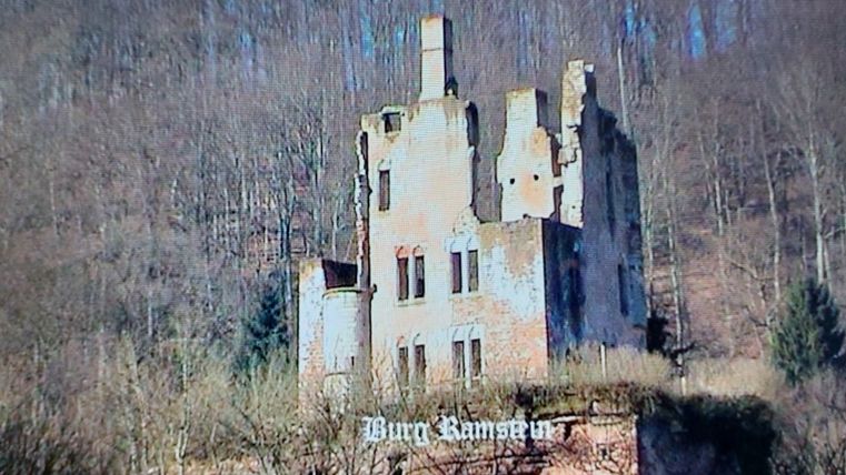 Eine alte Ruine auf einem Hügel, umgeben von Bäumen und sanften Hängen. Die Struktur des Gebäudes ist teilweise eingestürzt und zeigt historische Merkmale.