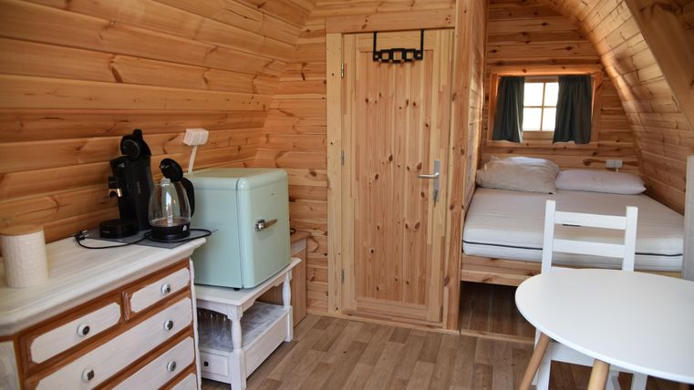 Ein gemütlicher Raum aus Holz mit einem Bett, einem kleinen Tisch und einem Kühlschrank. Es gibt auch eine Kaffeemaschine und Fenster mit Vorhängen.