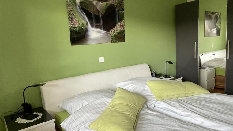 Ein modernes Schlafzimmer mit grünen Wänden und einem bequemen Bett. An der Wand hängt ein Bild von einem Wasserfall, das eine entspannende Atmosphäre schafft.