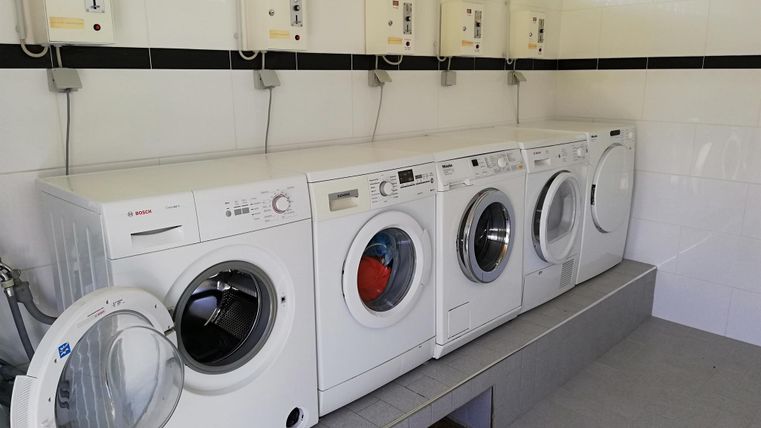 Eine Reihe von weißen Waschmaschinen in einem hellen Raum. An der Wand sind Steuergeräte installiert.