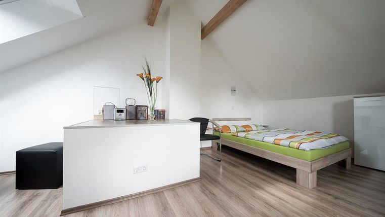 Ein modernes Schlafzimmer mit einem Bett, einem Schreibtisch und einem Stuhl. Der Raum hat helle Wände und Holzfußboden, mit einem gemütlichen und minimalistischem Design.