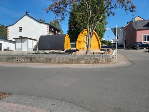 Zwei kleine, bunte Hütten stehen auf einer Kreisverkehrstraße, umgeben von Wohngebäuden. Der Himmel ist klar und blau, und es ist ein sonniger Tag.