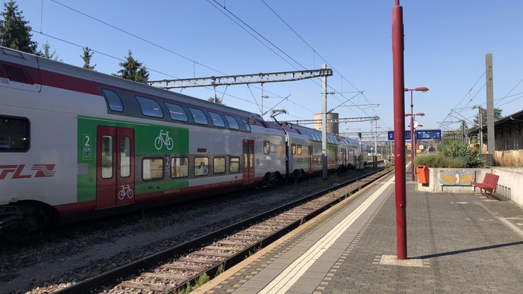 Ein Bahnhof mit mehreren Zügen auf den Gleisen. Die Umgebung ist hell und sonnig, mit einer klaren blauen Himmel.