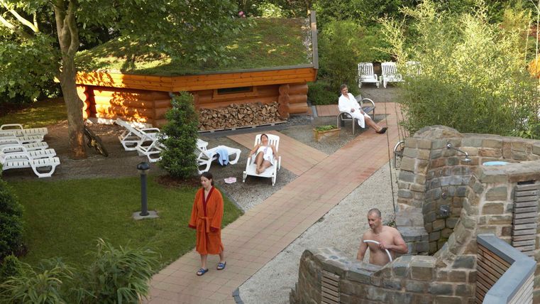 Ein entspannendes Spa-Gelände mit einer Sauna und Liegen. Einige Personen genießen die Ruhe in der Natur.