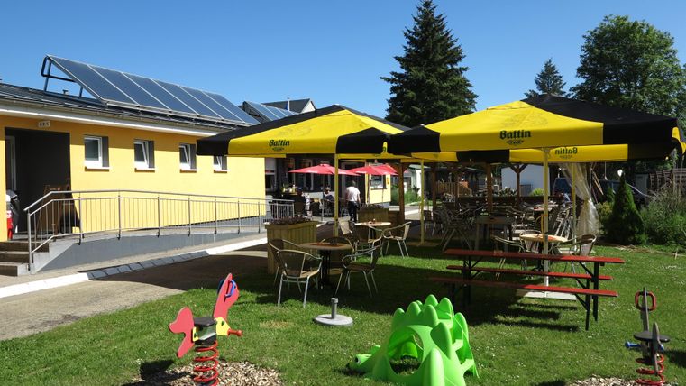 Ein einladender Außenbereich mit Sonnenschirmen und Möbeln. Die Umgebung ist grün und freundlich gestaltet.