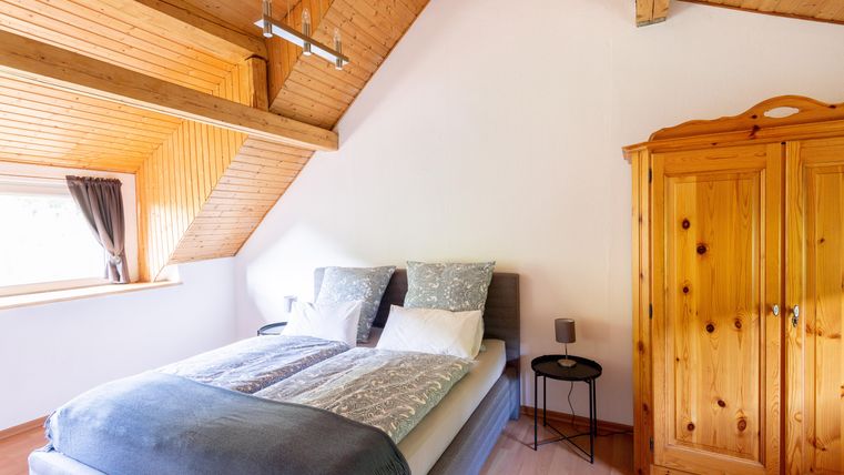 Ein gemütliches Schlafzimmer mit einem Doppelbett und Holzverkleidung. Ein Holzschrank und ein kleiner Nachttisch ergänzen die Einrichtung.