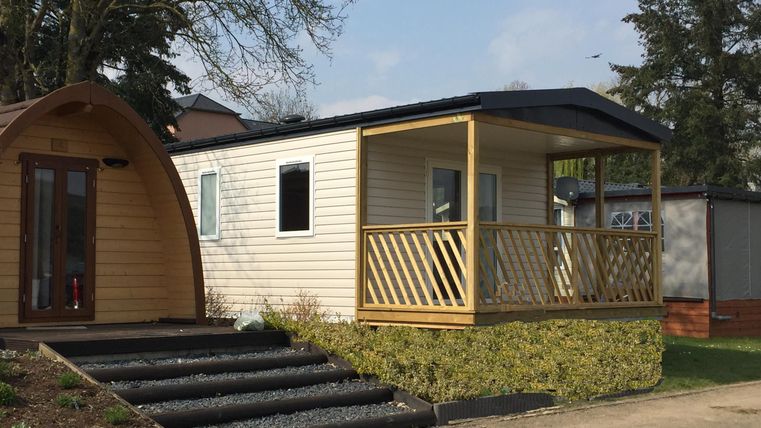 Ein modernes Ferienhaus mit Veranda und Garten. Daneben steht eine gemütliche Holzhütte.
