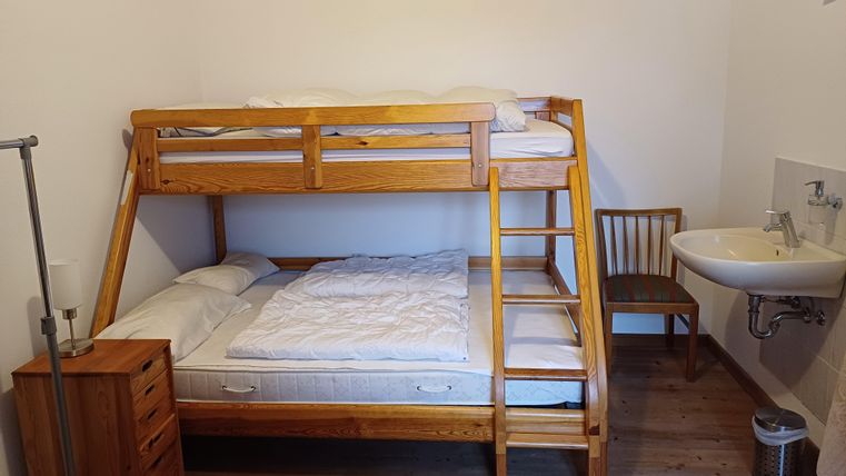 Ein schlichtes Zimmer mit einem Etagenbett aus Holz. Es gibt einen kleinen Tisch und ein Waschbecken in der Ecke.