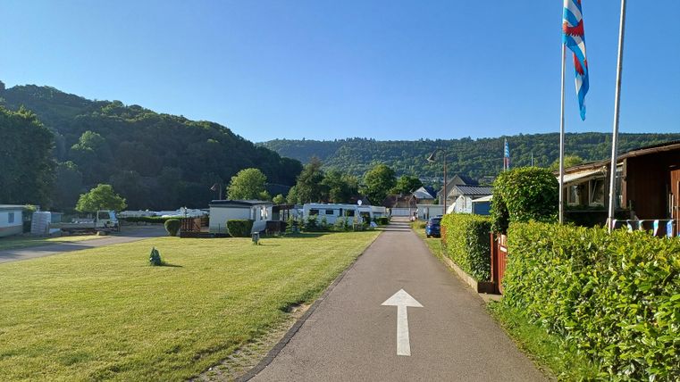 Ein ruhiger Campingplatz mit geraden Wegen und grünen Rasenflächen. Im Hintergrund sind Bäume und Hügel zu sehen.