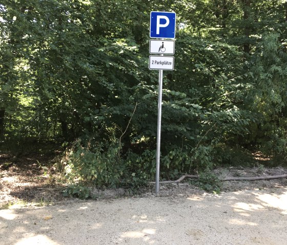 Un panneau de parking pour personnes handicap&eacute;es dans la for&ecirc;t. Il indique deux places de stationnement disponibles. Entour&eacute; d'une v&eacute;g&eacute;tation dense et d'arbres., &copy; TI Bitburger Land
