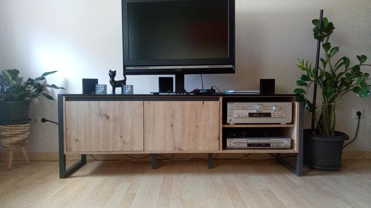 Ein modernes TV-Möbel mit einem großen Fernseher und Pflanzen daneben. Der Raum hat einen hellen, minimalistischen Stil.