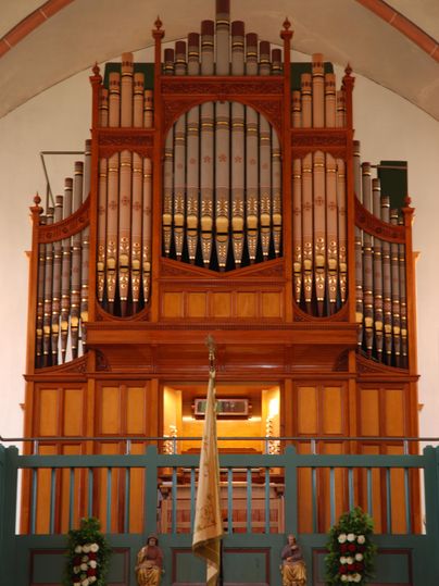 Eine beeindruckende Orgel in einem Kirchenraum. Die holzfarbene Konstruktion ist reich verziert und strahlt eine feierliche Atmosphäre aus.