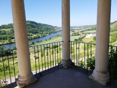 Ein Blick von einem Balkon mit Säulen auf einen Fluss und grüne Landschaften. Der Himmel ist klar und blau.