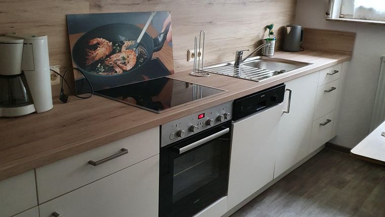 Eine moderne Küche mit hellen Schränken und Holzdetails. Sie ist gut ausgestattet mit einem Herd, einer Spüle und einem Kaffeekocher.