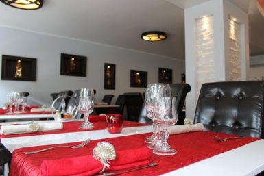 Ein elegantes Restaurant mit einem festlich gedeckten Tisch. Die rote Tischdecke und die stilvollen Stühle schaffen eine einladende Atmosphäre.