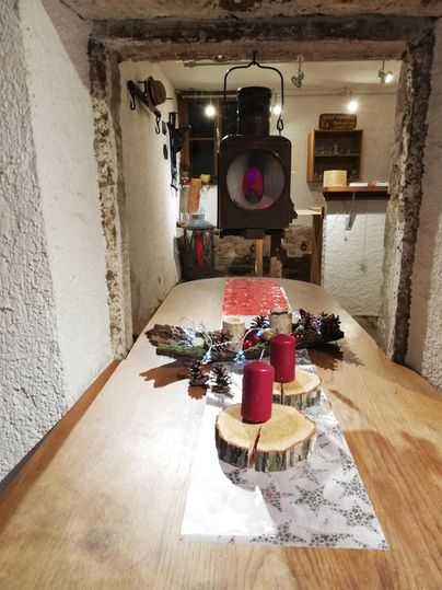 Ein rustikaler Tisch mit Holzscheiben und roten Kerzen. Im Hintergrund hängt eine altmodische Lampe an der Wand.