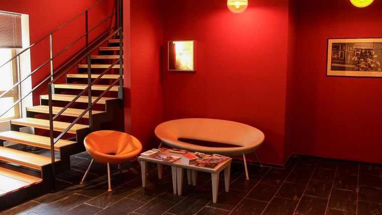 Ein modernes Wohnzimmer mit roten Wänden und stilvollen Möbeln. Die Treppe im Hintergrund verleiht dem Raum eine elegante Note.