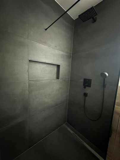 Eine moderne Dusche mit dunklen Fliesen und einer minimalistischen Ausstattung. Die Dusche hat eine praktische Nische und eine Regendusche.