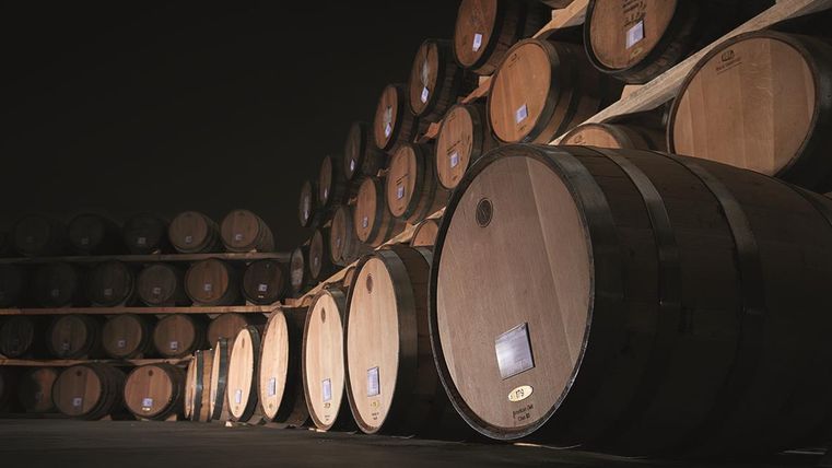 Ein Lagerraum mit mehreren Holzfässern, die übereinander gestapelt sind. Die Fässer sind gut beleuchtet und stehen an einer wandlosen Fläche.