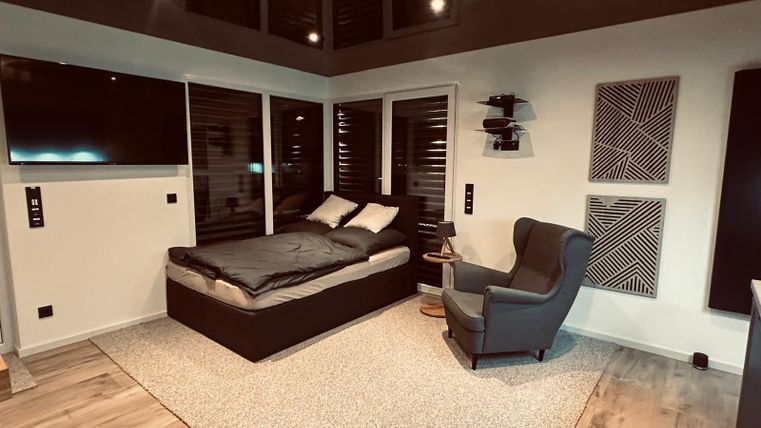 Ein modernes Schlafzimmer mit einem gemütlichen Bett und einem bequemen Sessel. Große Fenster lassen viel Licht herein und sorgen für eine einladende Atmosphäre.