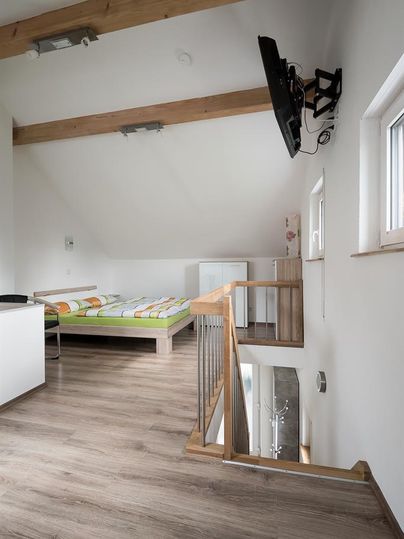 Ein helles Zimmer mit Holzdecken, einem Fernseher an der Wand und einem Doppelbett. Es gibt eine Treppe und einen kleinen Wohnbereich.