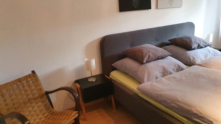 Ein gemütliches Schlafzimmer mit einem Doppelbett und Kissen. Neben dem Bett steht ein Stuhl und ein Nachttisch mit einer Lampe.