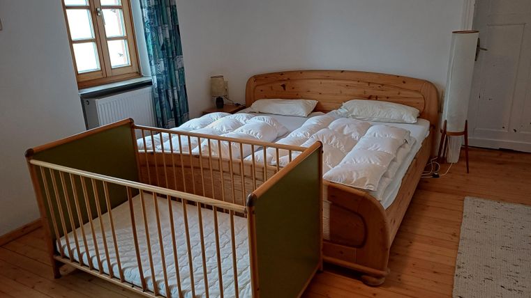 Ein gemütliches Schlafzimmer mit einem großen Bett und einem Babybett. Das Zimmer hat Holzböden und sanfte Farben.