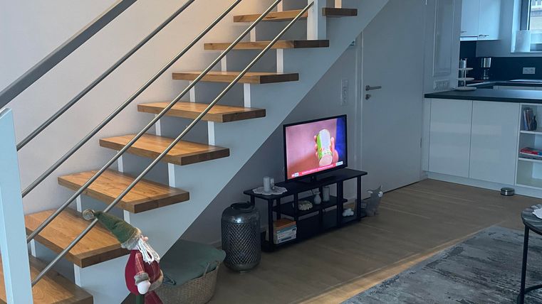 Vom Wohnzimmer aus führt eine hochwertige Holztreppe ins Obergeschoss zu den Schlafzimmern und dem Badezimmer. Die Treppe besticht durch hochwertige Verarbeitung und sorgt für ein stilvolles Wohngefühl.