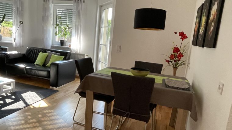 Ein modernes Wohnzimmer mit einem Essbereich. Der Tisch ist mit einem grünen Tuch und einer Blumendekoration geschmückt.