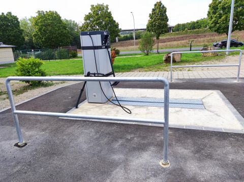 Eine moderne Tankstelle mit einer Säule und einem Schlauch. Der Bereich ist sauber und von grüner Landschaft umgeben.