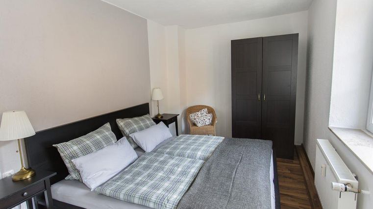 Ein gemütliches Schlafzimmer mit einem großen Bett und Kissen in grau und kariert. Es gibt einen Stuhl, eine Lampe und einen Kleiderschrank.