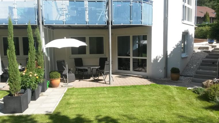 Ein schöner Garten mit einem gepflegten Rasen und modernen Pflanzen. Es gibt einen Tisch mit Stühlen und einen Sonnenschirm.