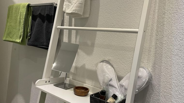 Ein modernes, weißes Regal mit Handtüchern und kosmetischen Utensilien. Das Regal steht an einer Wand und ist dekorativ angeordnet.