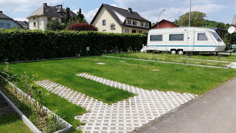 Ein grünes Freizeitgrundstück mit einem Wohnwagen. Im Hintergrund sind einige Häuser und ein Sportplatz zu sehen.