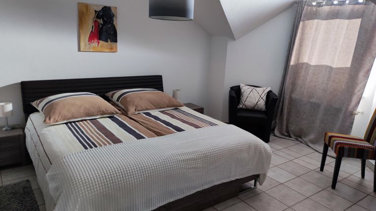 Ein gemütliches Schlafzimmer mit einem Doppelbett und modernen Möbeln. Es gibt ein Fenster mit Vorhängen und eine entspannende Sitzecke.