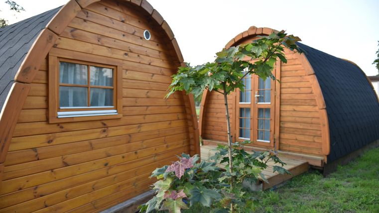 Zwei gemütliche Holzbungalows mit gewölbtem Dach stehen in einer grünen Umgebung. Ein kleiner Baum wächst zwischen ihnen.