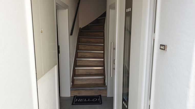 Ein heller Flur mit einer Treppe, die nach oben führt. Am Boden liegt ein Teppich mit dem Schriftzug "HELLO".