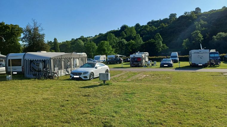 Ein schöner Campingplatz mit Wohnmobilen und Wohnwagen. Die grüne Wiese und die Bäume im Hintergrund vermitteln eine entspannte Atmosphäre.