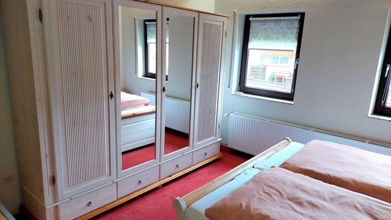Ein gemütliches Schlafzimmer mit einem großen Schrank und einem Doppelbett. Die Wände sind hell und es gibt zwei Fenster mit Blick nach draußen.